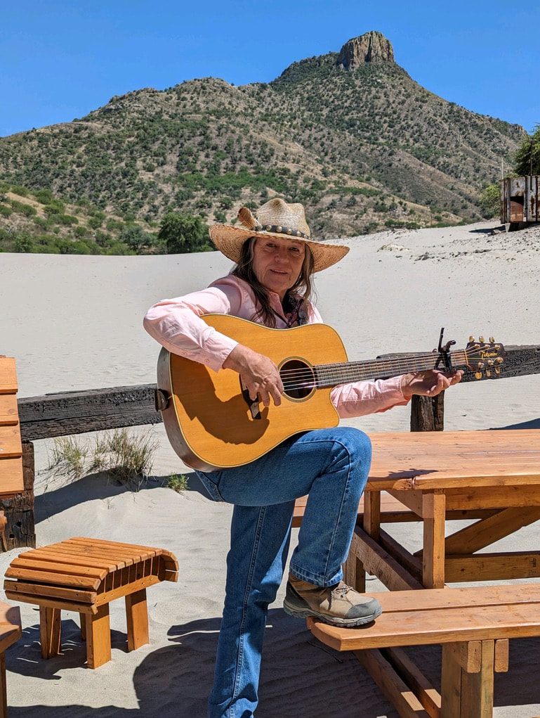 Caretaker Leslie Case poses with guitar by new donated picnic tables.