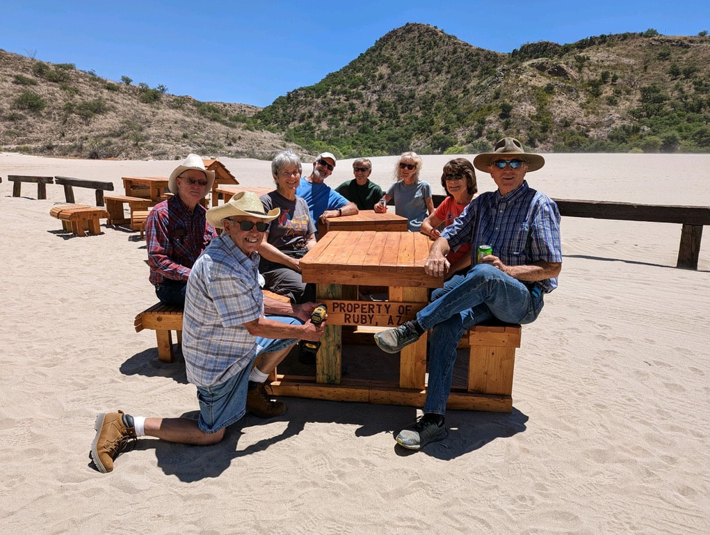 Group of people around newly donated picnic table in Ruby's sand tailings scenery